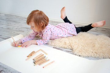 Girl draws with colored pencils lying on the floor