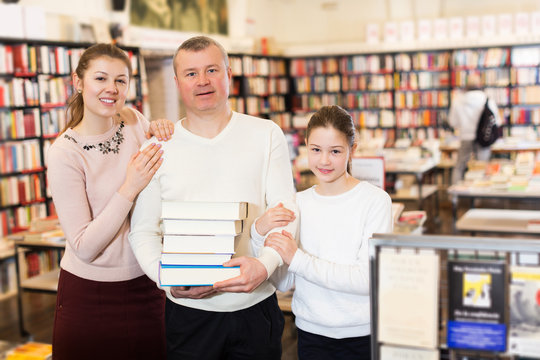 parents and girl standing with stack of books