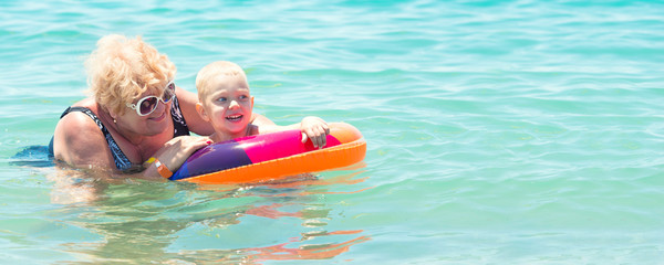 Grandmother and little grandson swim in the sea.The baby in the bouncy multicolored circle.Summer...