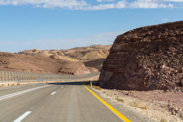 Asphalt road and fence wall on boarder with Egypt in desert Negev, Israel, road 12, transport infrastructure in desert, scenic mountains route from Eilat to north of Israel
