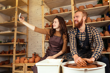 a bearded man and a young woman mold a vase of clay on a potter's wheel and make a selfie on the phone in a pottery workshop. potter, clay, vase, pottery workshop. master and student