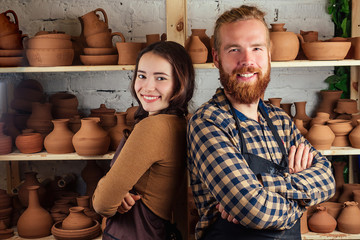 a bearded man and a young woman stand beside the rack with vases and pots of clay. Potter, clay, vase, pottery workshop