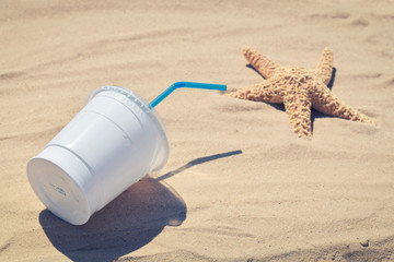 A cup of disposable plastic on the beach. The concept of plastic contamination