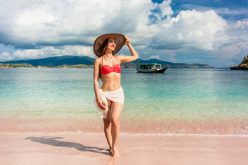Fototapeta premium Fashionable young woman with a perfect body smiling while posing outdoors during summer vacation at Pink Beach, pink, in Komodo Island, Indonesia 