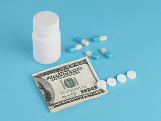 Pharmaceutical pills, hundred dollar bill and bottle on blue background. Concept business and drugs.