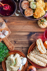 Traditional home-cooked dishes in Ukrainian cuisine on a wooden table - borsch, vareniki, pampushki with garlic, lard, pancakes, potatoes, vvar, top view, copy space
