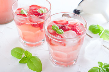 Fresh cool summer drink with strawberries and green basil in glass glasses on white table, horizontal, copy space