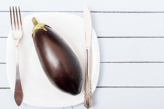 One whole eggplant on white plate. Fresh organic fruit. Healthy nutrition concept