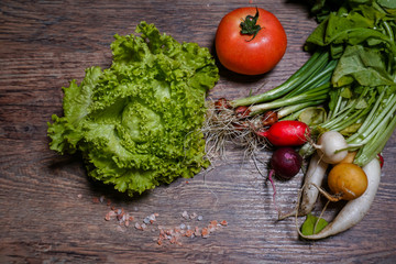 Fresh home-made green lettuce, tomato and colorful radishes on a wooden background. Detached from the home garden.