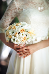 Beauty wedding bouquet from chamomile and beige roses in bride's hands, close - up