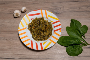 Delicious homemade risotto with spinach, onion and carrots. Decorated with garlic. On a wooden background.
