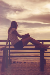Fototapeta premium Silhoutte of a girl while sitting on a bench and looking the ocean / sea scenery.