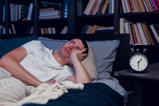 Image of man with insomnia lying in bed next to alarm clock