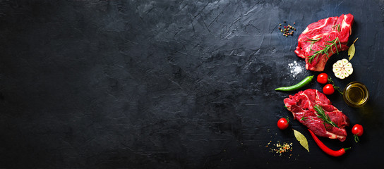 Raw meat, beef steak on a stone cutting board with rosemary, spices, salt, oil, cherry tomatoes,...