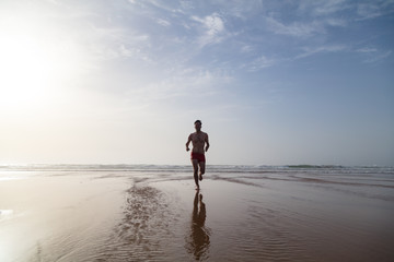 Young man in swimming trunks running away from sea on the beach