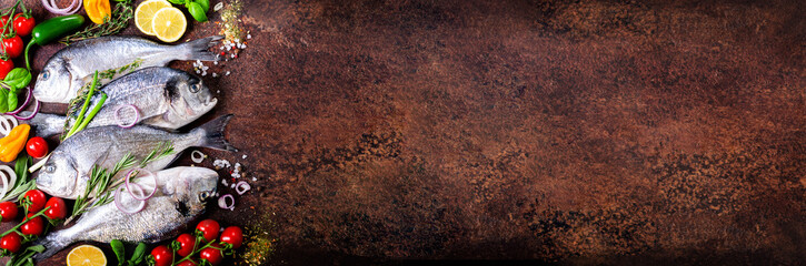Fresh uncooked fish, dorado, sea bream with lemon, herbs, vegetables and spices on rustic background. Top view. Banner