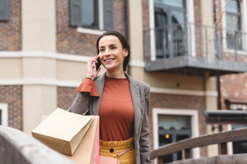 smiling woman walking after shopping and talking by smartphone