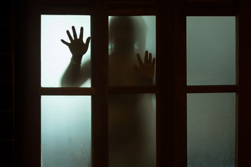 Horror woman behind the window glass in black and white. Blurry hand and body figure abstraction.Halloween background.