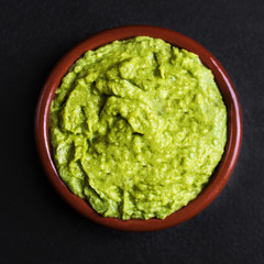 Guacamole spread  in clay bowl on a black background. Avocado sauce. Top view with copy space.