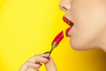 a young woman uses a red chili pepper like lipstick on yellow background