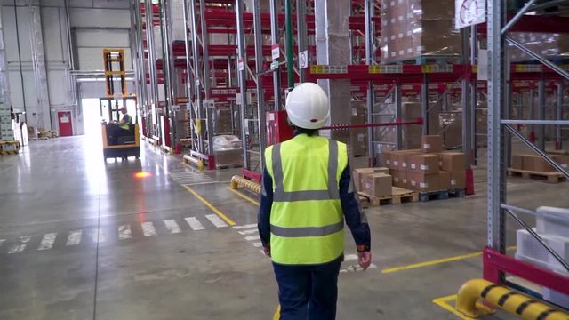 female warehouse worker with helmet and safety vest. Clip. Young female in protective uniform, helmet and eyeglasses holding walkie-talkie while working at plant