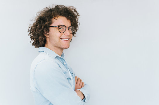 Profile horizontal view portrait of handsome young male with curly hair, wearing denim blue shirt and round trendy spectacles, looking to the camera. Copy space for advertisement. People race concept.