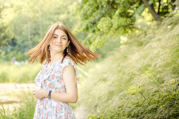 Fototapeta na wymiar Beautyful stylish young fashionable smolling woman with long hair turns on the background of nature.