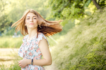Beautyful stylish young fashionable smolling woman with long hair turns on the background of nature.