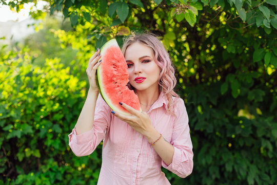 Beautiful young woman with pink hair enjoying watermelon