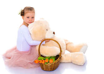A little girl with a basket of flowers and a teddy bear is sitti