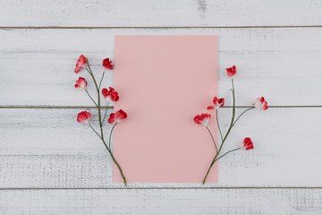 Blank pink card decorate with red paper flowers on white wood background 