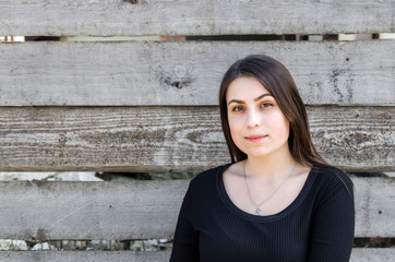 Portrait of a beautiful young brunette girl against a wall background of coarse-hewn gray boards.