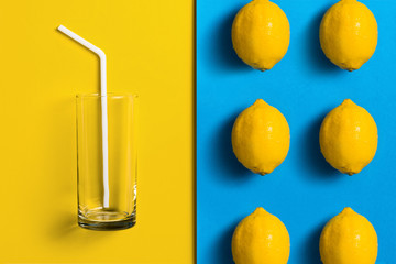 Lemons on split colored background with glass and straw.