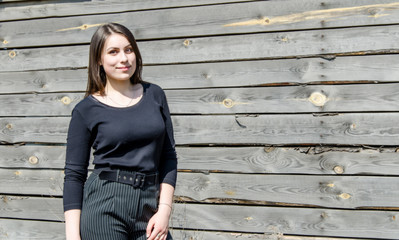 Fototapeta premium Portrait of a beautiful young brunette girl against a wall background of coarse-hewn gray boards.