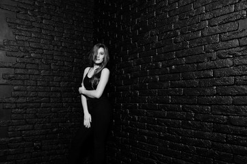 Handsome brunette girl wear on black, posing at studio against dark brick wall. Studio model portrait.