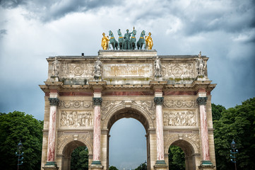 Fototapeta premium Arc de triomphe du carrousel in paris, france. Arch monument and green trees on cloudy sky. Architectural symbol of peace victory and fame. Vacation and wanderlust in french capital