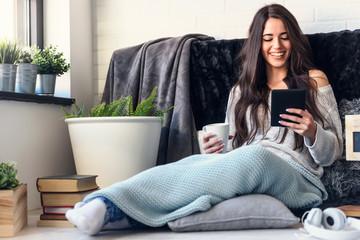 Beautiful young woman reading e book reader at home surrounded by books