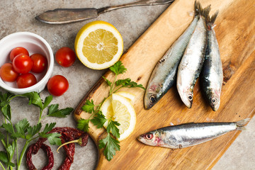 Sardinas con tomates, limón y perejil sobre tabla de madera rústica. Vista superior y de cerca