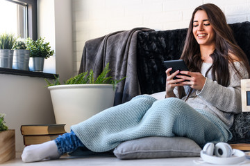 Beautiful young woman reading e book reader at home surrounded by books