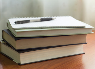 stack of books and a notebook with a pen on the table