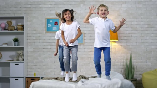 Group of three active children of primary school age having fun when jumping on bed, slow motion