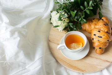 Tea with lemon and croissants for breakfast. Roses flowers bouquet. Eating in Bed