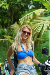 Fototapeta na wymiar beautiful blonde girl in sunglasses sitting on motorbike and smiling at camera