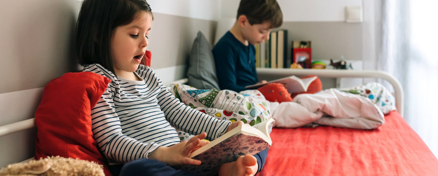 Girl and boy reading a book each sitting on the bed. Selective focus on girl in foreground