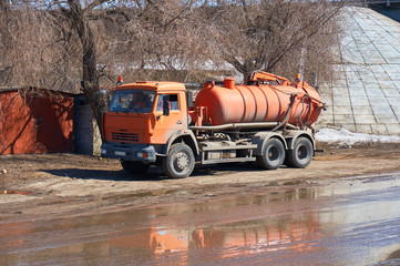 A water truck of orange color is standing by the road.