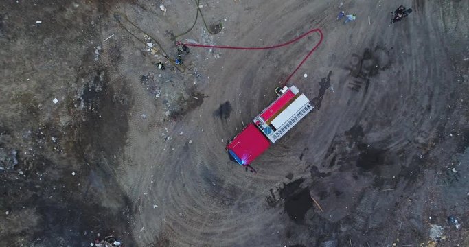 Aerial view of red fire truck with led light. Burning dump. Aerial view from drone of dense smoke poured in air and red fire-truck on fireground.