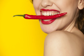 Young sexy woman holding a chili with her teeth on white background