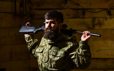 Masculinity concept. Man, gamekeeper with beard wears camouflage clothing, carries rifle on...