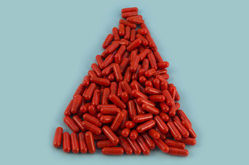 Medical capsules of red color, laid in the shape of an isosceles triangle on a blue background.