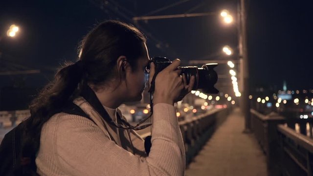 Photographer traveller takes shot standing on city bridge with traffic at night time